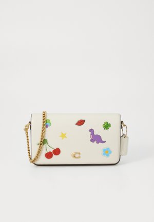 Weiße Handtasche aus Kunstleder mit goldener Kettenriemen, verziert mit bunten Aufnähern, darunter Kirschen, ein Dinosaurier und eine Blume.