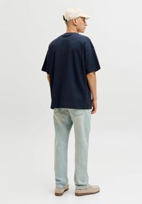 Marinbl�å bomullst-shirt med korta ärmar och lös passform, bärs med ljusblå jeans i denim och beige skor, avslutad med en ljus keps.