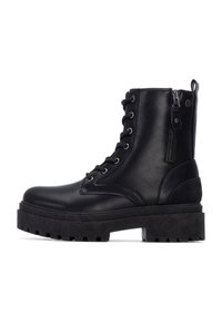 Botas de cuero negro hasta el tobillo con cordones en la parte frontal, cremallera lateral, suela gruesa negra y suela con textura antideslizante. Acabado brillante y diseño de punta redonda.