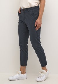 Pantalons en coton chino bleu marine avec une coupe slim, poches latérales et ourlets retroussés, associés à des baskets blanches et un haut de couleur claire.