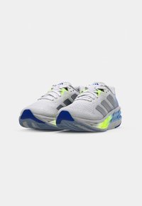 Baskets de sport blanches avec des accents gris, semelle bleue et détails en jaune fluo. Tige texturée et semelle superposée pour un amorti et un soutien.