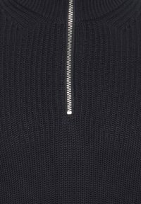 Schwarzer Strickpullover mit hohem Kragen und silbernem Reißverschluss. Verfügt über ein strukturiertes Muster, das die Handwerkskunst hervorhebt.
