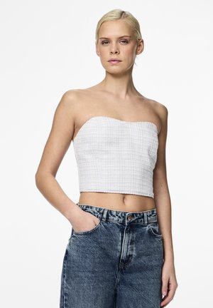 Biely, textúrovaný crop top bez ramienok s priliehavým strihom, v kombinácii s vysokými modrými džínsami s vybledlým povrchom a prednými vreckami.