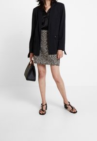 Schwarzer Blazer über einer satin schwarzen Bluse, kombiniert mit einem Minirock im Leopardenmuster. Accessoires: schwarze Handtasche und schwarze Riemchen-Highheels.