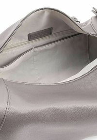 Interno di una borsa in pelle grigia con una texture liscia, dotata di una tasca con cerniera e di un compartimento aperto. Bordi cuciti e cerniera metallica.