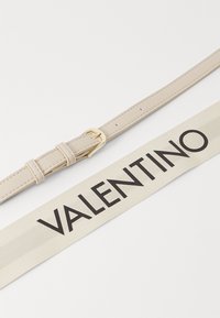 Leren riem in lichtbeige met een gouden gesp. Vergezeld door een crèmekleurige stoffen band met "VALENTINO" in vetgedrukte zwarte letters.