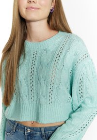 Maglione di colore verde menta lavorato a maglia con motivo a treccia, design cropped e maniche texturizzate. Abbinato a jeans in denim a vita alta.