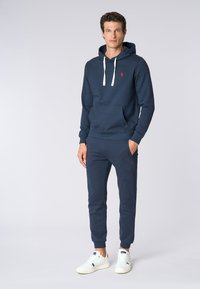 Set di felpa con cappuccio e pantaloni blu navy realizzato in misto cotone; presenta una tasca frontale, cappuccio con cordini e accenti del logo rosso, abbinato a sneakers bianche.