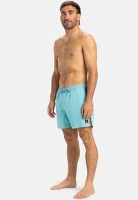 Maillots de bain bleu clair avec une taille élastique, un cordon de serrage, des accents de rayures sur les côtés en orange, et une petite écusson logo sur la cuisse.