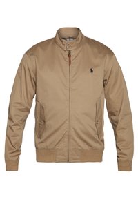Beige Bomberjacke mit Stehkragen, Frontreißverschluss, Seitentaschen und Rippbündchen. Verfügt über ein kleines dunkles Logo auf der linken Brust.
