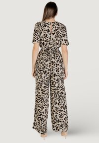 Mono con estampado animal en beige, con mangas cortas, piernas anchas, cintura ceñida con cinturón y detalle de abertura en la parte posterior. Textura de tela suave.