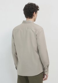 Hellbeige Langarmhemd mit Kragen, knöpfbaren Manschetten und einer glatten, matten Textur. Verfügt über einen geraden Schnitt und ein Rückenpasse-Design.