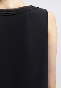 Top senza maniche nero caratterizzato da una texture morbida e liscia, con un collo leggermente trasparente e cuciture ordinate e semplici lungo i bordi.