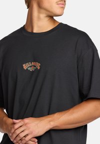 Camiseta de algodón negra con un logo multicolor que presenta acentos en rojo, verde y blanco. Corte relajado, mangas cortas y cuello redondo.