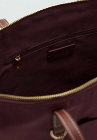 Bordeaux canvas tote bag interieur met een gouden rits, met een ritsvak en een leren labelaccent. Gladde textuur en minimalistisch ontwerp.