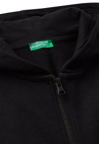 Felpa nera con zip e cappuccio realizzata in tessuto morbido, con zip frontale. Include un'etichetta verde con la scritta "United Colors of Benetton."