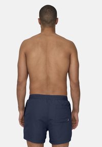 Bañador navy con cintura elástica y bolsillo trasero, confeccionado en una tela ligera y suave. Usado por un modelo masculino visto desde atrás.