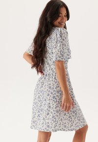 Abito floreale con maniche corte, caratterizzato da uno sfondo bianco e una stampa floreale blu. Vita arricciata, design alla lunghezza del ginocchio, tessuto leggero.