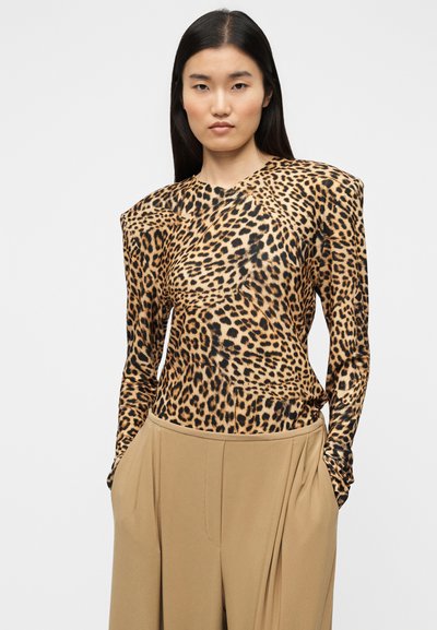 Μπλούζα με λεοπάρ σχέδιο και μακρύ μανίκι με δομημένους ώμους, φτιαγμένη από λείο ύφασμα, συνδυασμένη με μπεζ πλισέ παντελόνι με ψηλή μέση.
