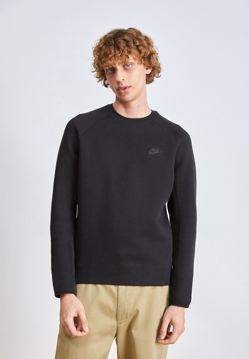 Sweat-shirt noir en tissu doux, avec des manches raglan longues, un col rond et un logo discret sur la poitrine.
