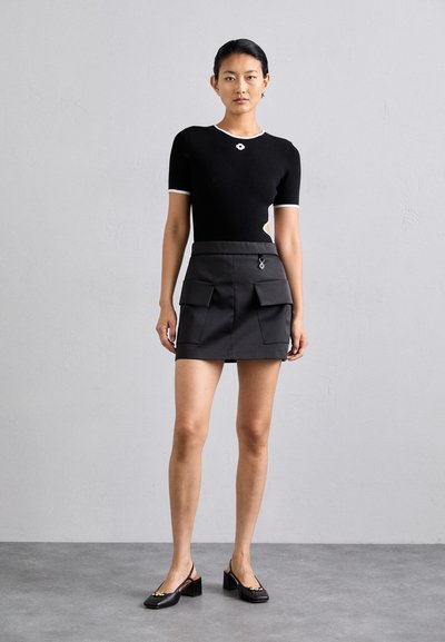 Schwarzes kurzärmliges Top mit weißem Saum und floralem Schmuck; kombiniert mit einem dunkelgrauen Minirock mit Fronttaschen und silberner Hardware.