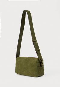 Πράσινη τσάντα χιαστί από σουέντ με ορθογώνιο σχήμα, ρυθμιζόμενο ιμάντα και φερμουάρ σε χρυσό τόνο. Ομαλή υφή και λιτές λεπτομέρειες εξαρτημάτων.