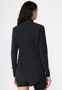 Schwarzer Langarmpullover mit Stehkragen, aus strukturiertem Stoff und mit stylischem Saum, kombiniert mit dunklen Sportshorts.