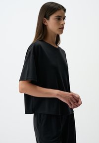 Zwarte katoenen t-shirt met een ontspannen pasvorm, korte mouwen en een ronde halslijn. Textuurstof met subtiele stikseldetails.