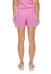 Rosafarbene Baumwollshorts mit einem elastischen Bund, die eine entspannte Passform und eine glatte Textur aufweisen. Getragen mit hellen Sandalen.