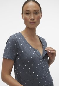 Grå kortärmad topp med stjärnmönster, med v-ringning och knapplist framtill. Mjuk tyg med en slät textur.