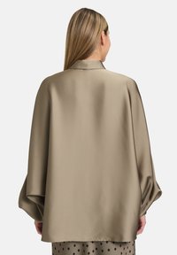 Blusa con cappuccio e vestibilità ampia in morbido satin color taupe, con spalle scese e una consistenza liscia e fluida.