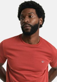 Red cotton crew neck t-shirt with short sleeves, featuring a small embroidered logo on the chest and a smooth, untextured surface.