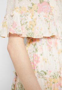 Robe fleurie à manches volantées, en tissu léger aux couleurs pastel — rose, jaune et vert — avec une surface texturée.