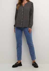 Blouse navy avec un motif géométrique crème, boutonnage sur le devant et manches longues, assortie à un jean slim bleu clair et des mocassins noirs.