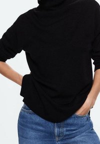 Maglione a collo alto nero in morbido tessuto a maglia, con maniche lunghe e vestibilità rilassata, abbinato a jeans azzurri a vita alta.