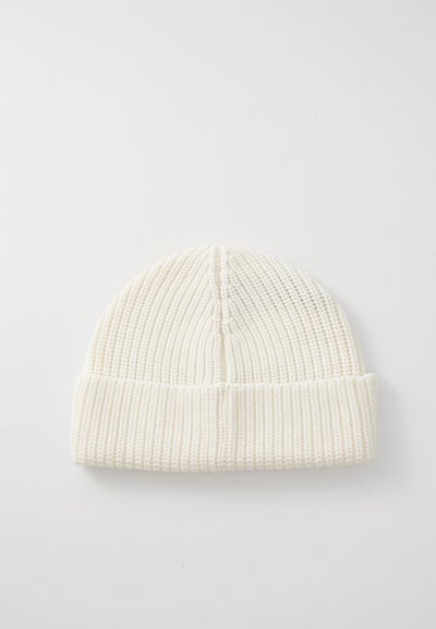 Balts adīts beanie ar ribota raksta un salocītu aproci, novietots plakans uz balta fona.