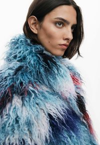 Faux-Fur-Mantel in einer Mischung aus Blau, Pink und Schwarz; lange, wellige Textur mit hohem Kragen für zusätzliche Wärme.