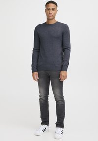 Donkergrijze gebreide sweater met een ronde hals, gecombineerd met vervaagde zwarte jeans en witte sneakers met drie zwarte strepen.