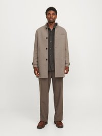 Pelēks vilnas mētelis ar augstu apkakli, pogu aizdari un krūšu kabatu, uzvilkts virs tumša krekla un bēšām biksēm. Izskatu pabeidz brūnas kurpes.