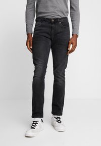 Black denim jeans with a slim fit, featuring a button closure, front pockets, and subtle fading. Paired with white sneakers.