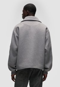 Šedá bunda ze směsi vlny s velkým límcem, povolenými rameny a žebrovanými manžetami, s uvolněným střihem a jemnými švy.