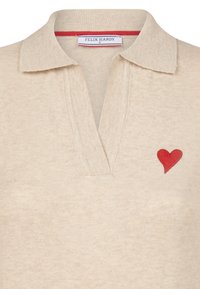 Beige gestricktes Poloshirt mit Kragen, versehen mit einem roten gestickten Herzen auf der linken Seite und einem kontrastierenden inneren Kragenband.