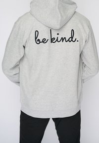 Sudadera gris con un acabado texturizado, que presenta una frase bordada en negro "sé amable" en la parte posterior. Incluye una capucha con cordón y puños acanalados.