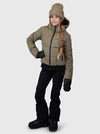 Menina jovem com um gorro bege e casaco, calças pretas e luvas, de pé com uma mão na cintura contra um fundo simples.