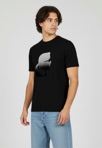 Czarny t-shirt z krótkim rękawem z szarym gradientowym nadrukiem sylwetki. Projekt z okrągłym dekoltem, gładką strukturą, zestawiony z jasnoniebieskimi dżinsami.