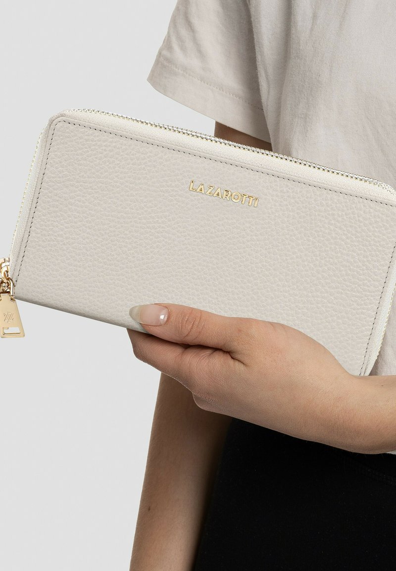 Billetera de cuero blanco con superficie texturizada, logo dorado "LAZAROTTI", cierre de cremallera y pequeño charm en forma de triángulo dorado.