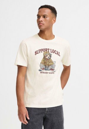 Crèmekleurig katoenen t-shirt met een afbeelding van een luiaard in een hoodie, vergezeld van de tekst "STEUN LOKALE STRAATKATTEN" in vet bordeauxrode letters.