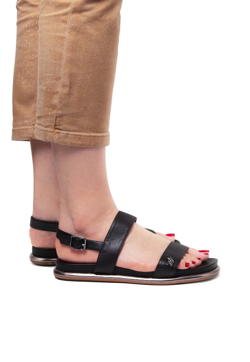 Svarta lädersandaler med breda remmar och spänne, med en platt sula och metallisk trim. Tårna är målade röda.