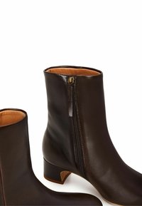Stivaletti in pelle marrone con zip laterale, dotati di un tacco basso e di una superficie liscia. Internamente foderati in materiale beige chiaro.