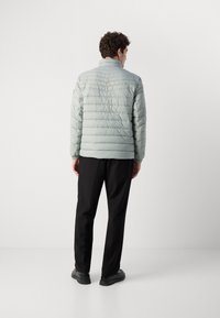 Light blue quilted puffer jacket with a standing collar, ribbed cuffs, and a straight hem, paired with black trousers and shoes.
